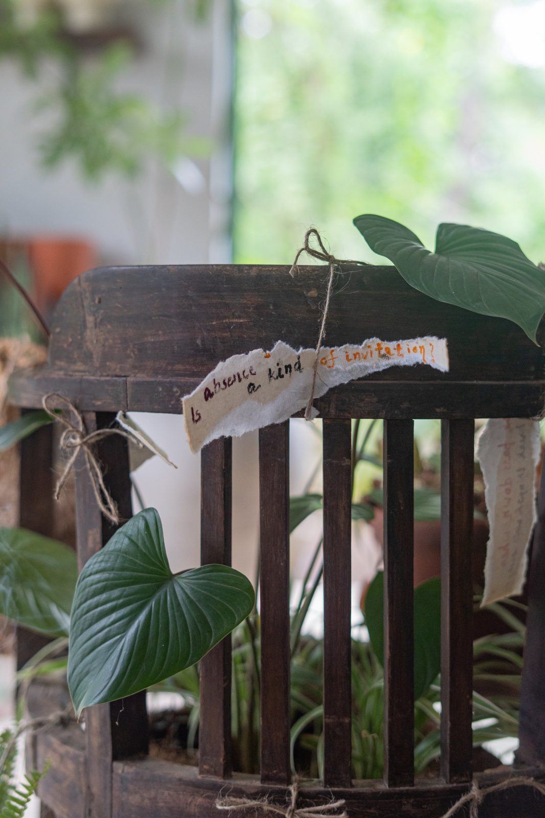 Detail of the chair back with a torn paper note tied on with jute, reading: Is absence a kind of invitation?